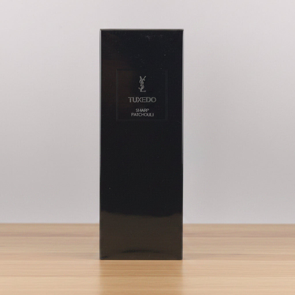 A tall, glossy black rectangular box for Yves Saint Laurent Tuxedo Shamp Parfums, featuring the silver YSL logo and brand name on the front, set against a neutral light gray background.
