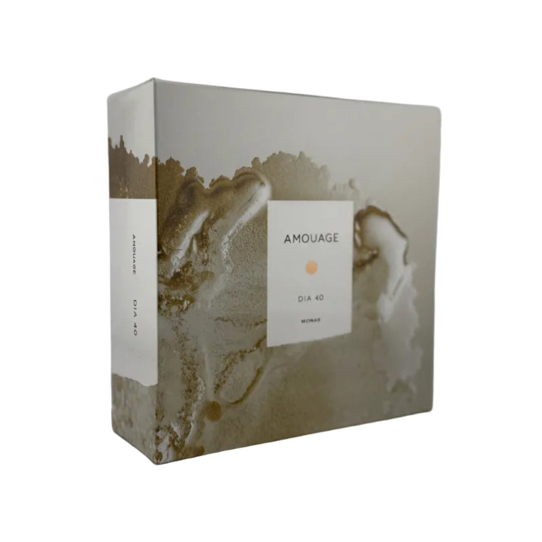 A rectangular product box with a metallic gold and silver abstract geode or marble pattern, featuring a white label on the front that reads 'AMOUAGE' and 'DIA 40'.