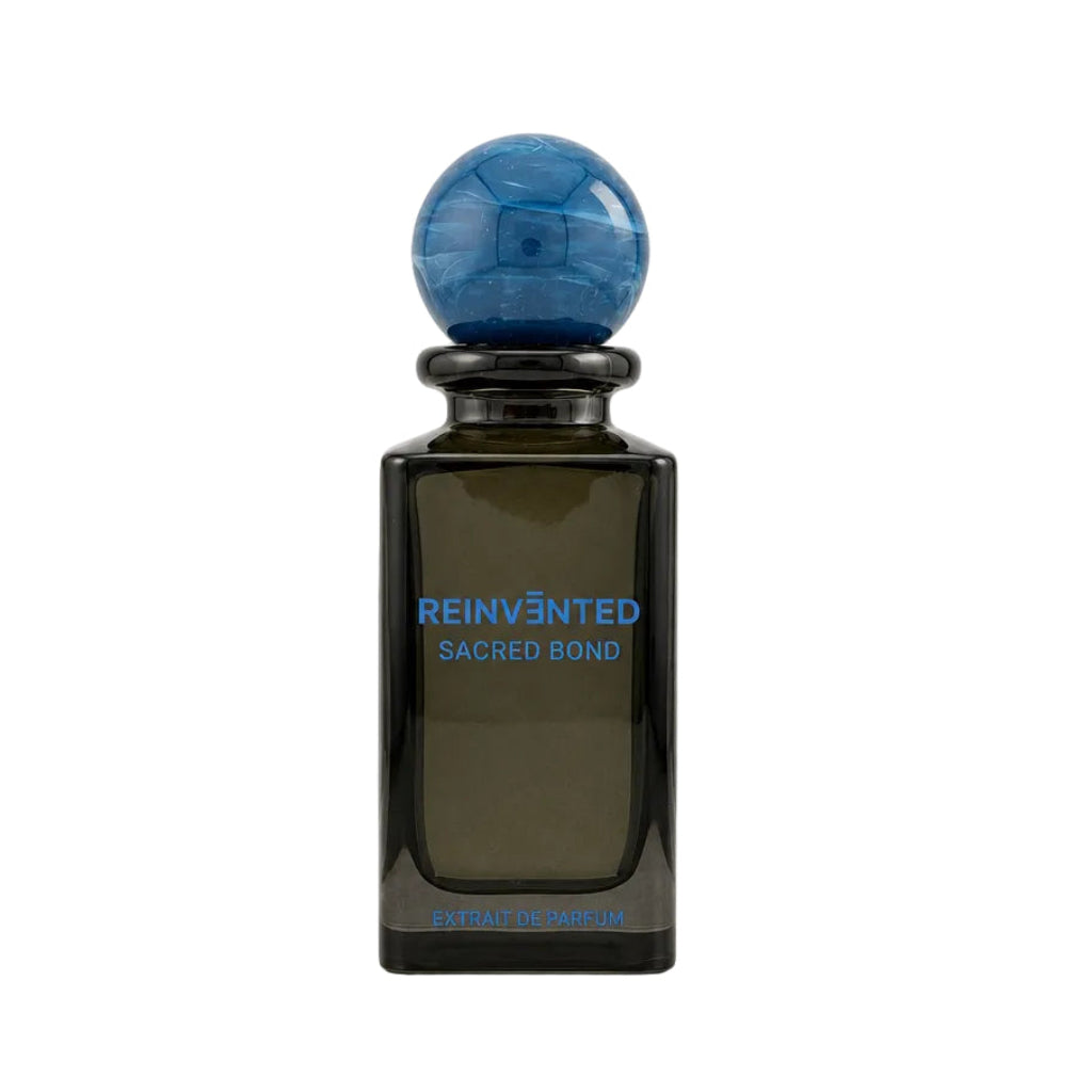 A dark amber glass bottle with a spherical blue cap, featuring blue text that reads 'REINVANTED SACRED BOND' on the front, set against a plain light gray background.