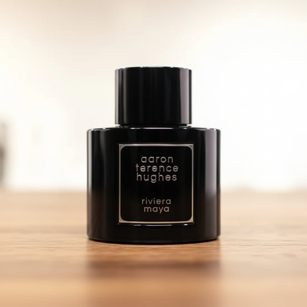 Black perfume bottle with 'aaron terence hughes' branding on a reflective surface.