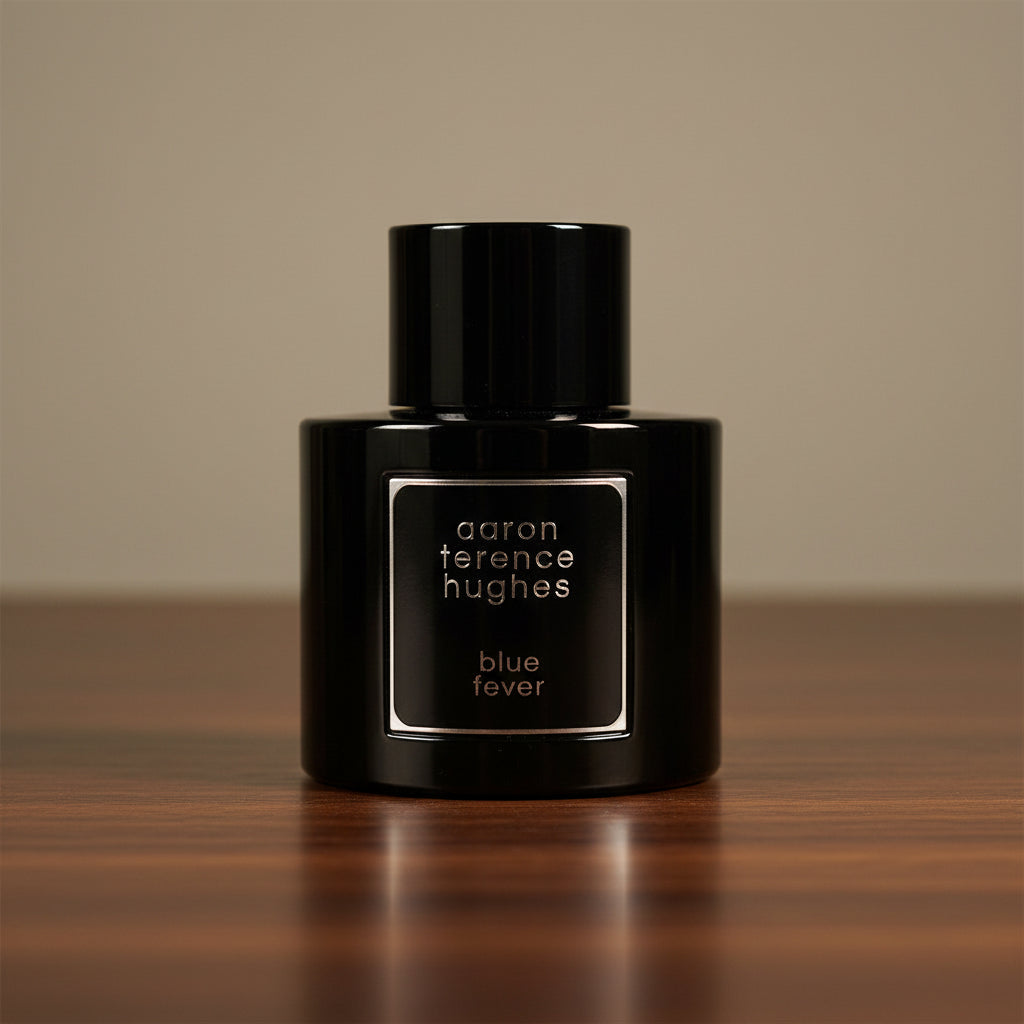 Black perfume bottle labeled 'aaron terence hughes blue fever' on a reflective surface with a blurred background.