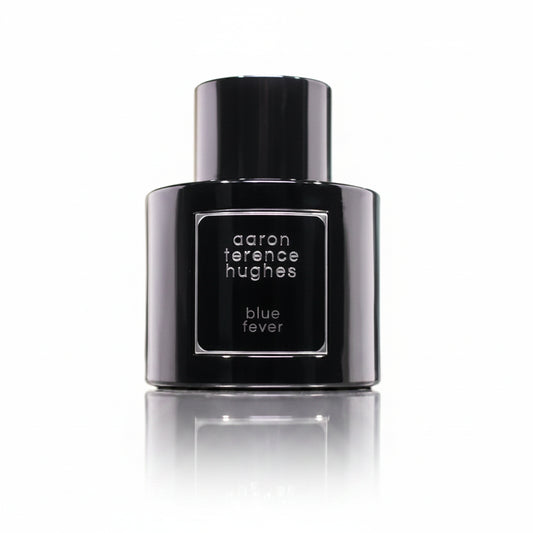 Black perfume bottle labeled 'aaron terence hughes blue fever' on a reflective surface with a blurred background.