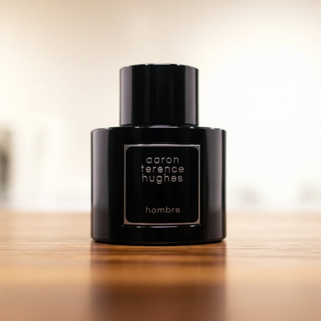 Black perfume bottle labeled 'aaron terence hughes hombre' on a reflective surface with a blurred background.