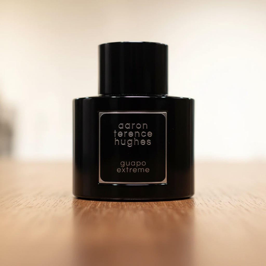 Perfume bottle labeled 'aaron terence hughes guapo extreme' on a reflective surface with a blurred background.