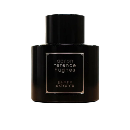 Perfume bottle labeled 'aaron terence hughes guapo extreme' on a reflective surface with a blurred background.