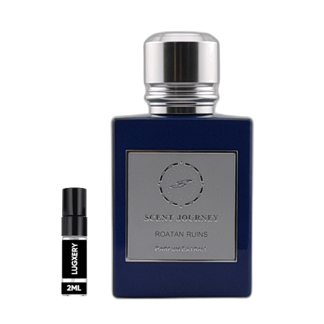 A dark blue rectangular perfume bottle with a silver cap and a silver front label reading 'SCENT JOURNEY ROATAN RUINS', shown next to a small black 2ml sample spray vial labeled 'LUXURY'.